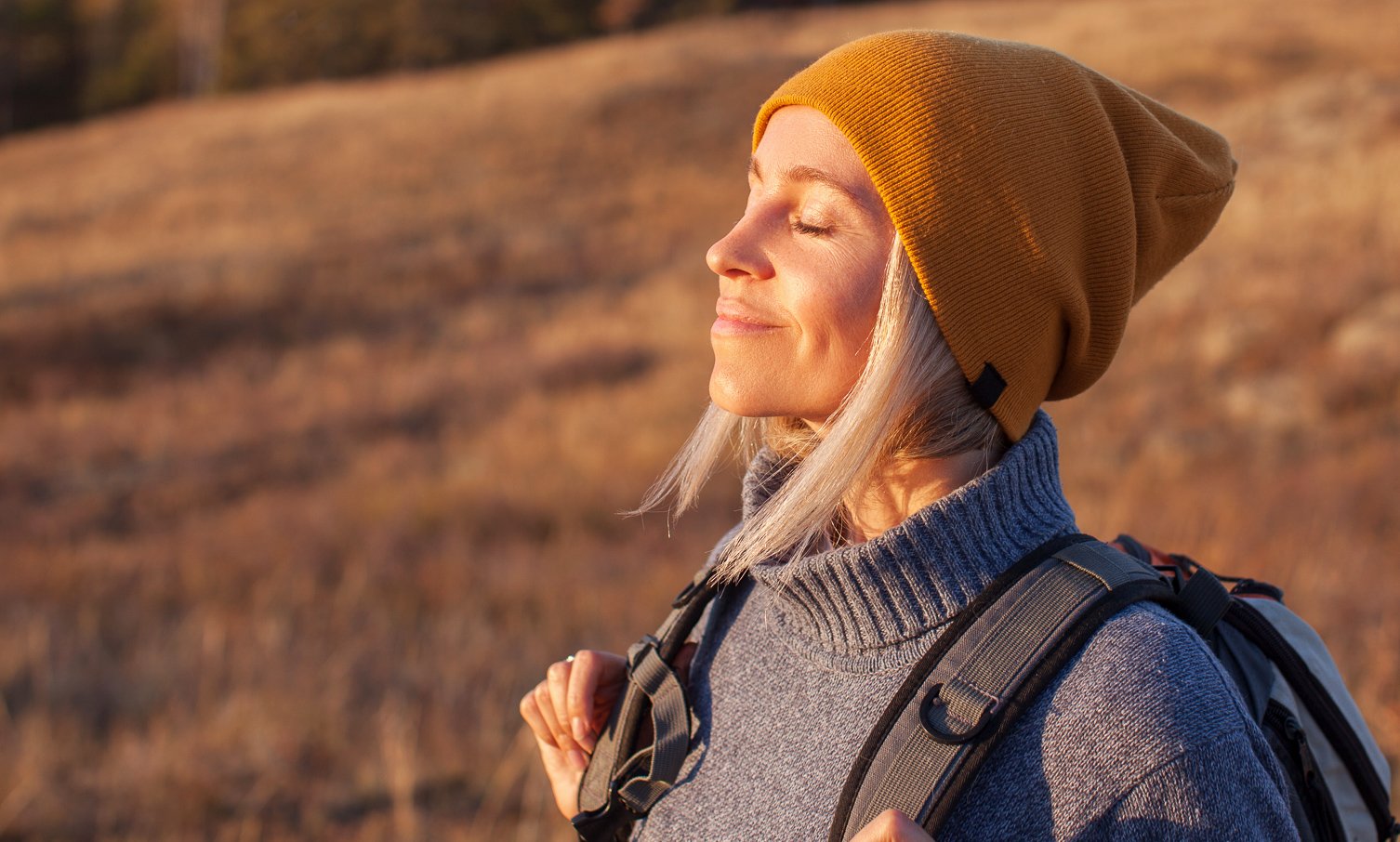 Smiling woman in a yellow beanie enjoying the sun during a hike in a golden field