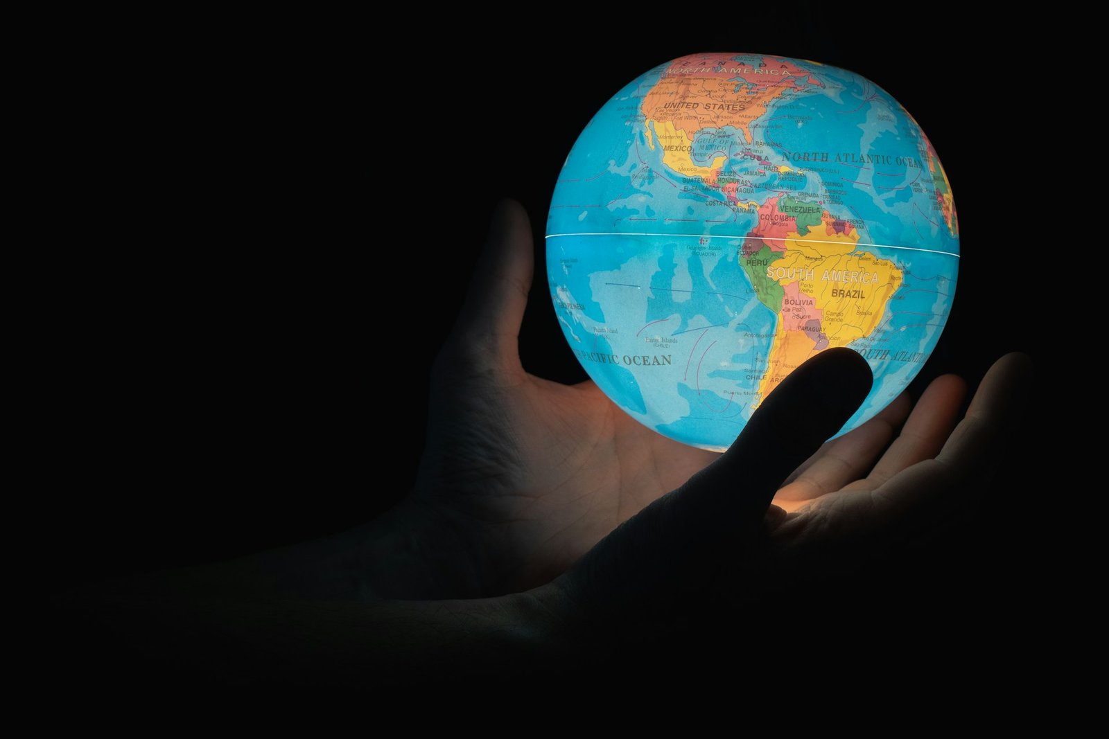 Hands holding a glowing globe in the dark, highlighting the Americas