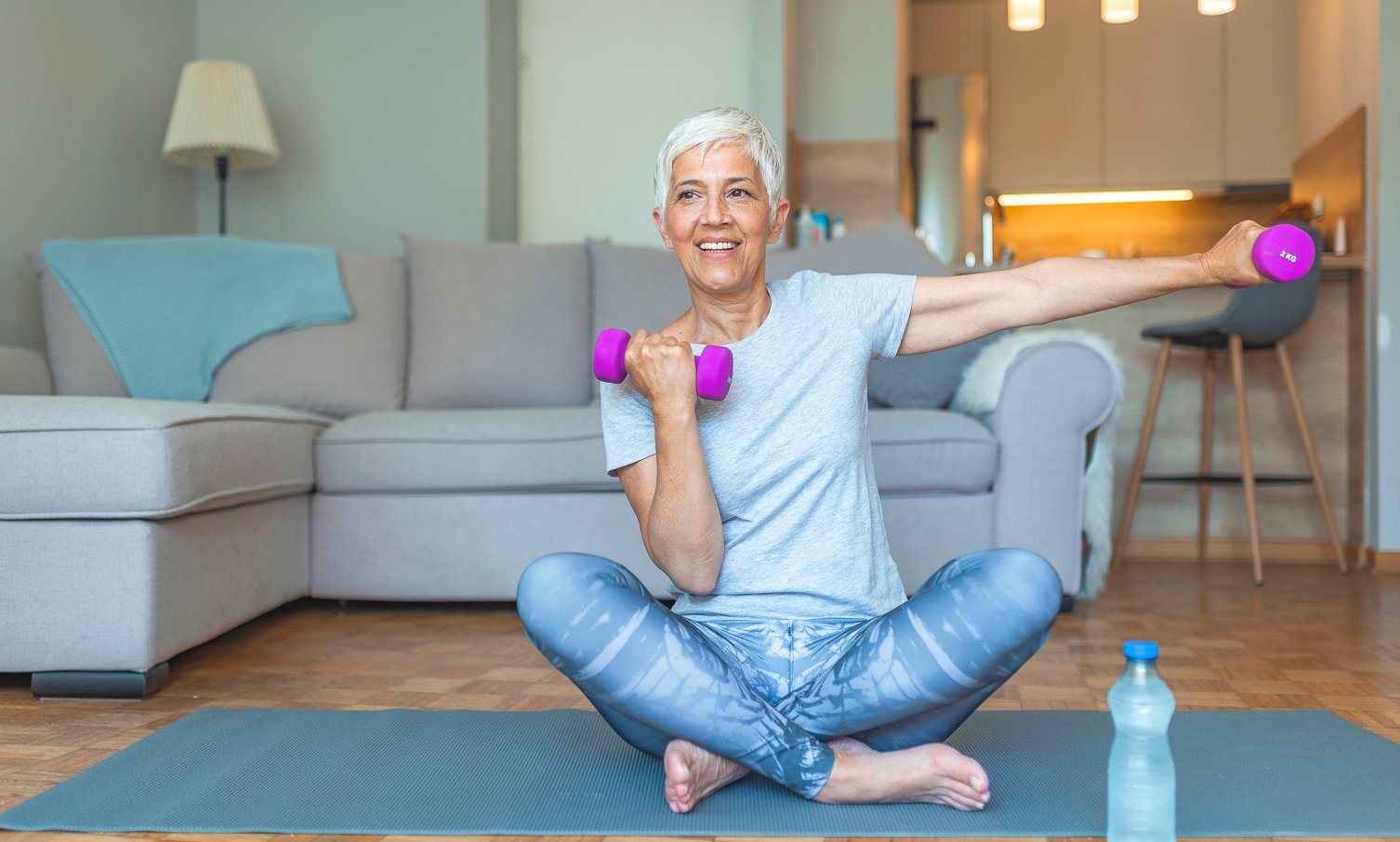 enior woman exercising with dumbbells at home. Portrait of an older woman in sportswear exercising with dumbbells indoors at home. Senior lady smiling at the camera whilst using dumbbells