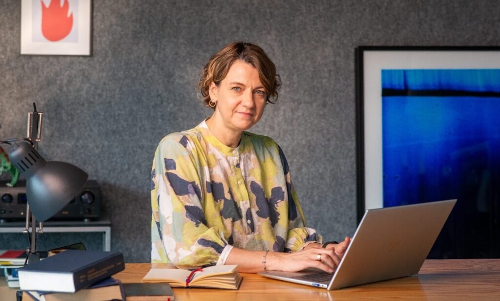 Jura_Lasas_sitting_by_the_table_typing_smiling_colorful_shirt_landscape_web-aspect-ratio-1506-906