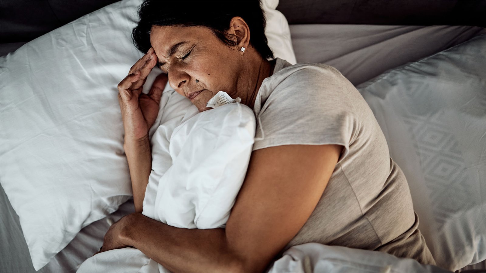 Woman sleeping uncomfortably with hand on forehead.