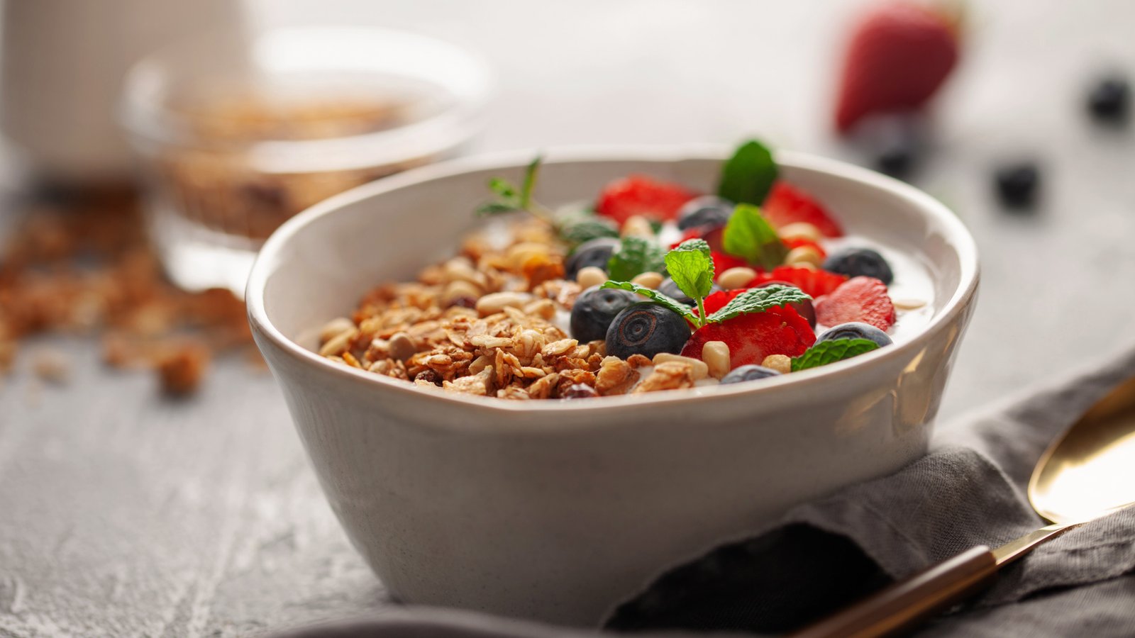 Bowl of yogurt topped with granola, blueberries, sliced strawberries, nuts, and fresh mint leaves.