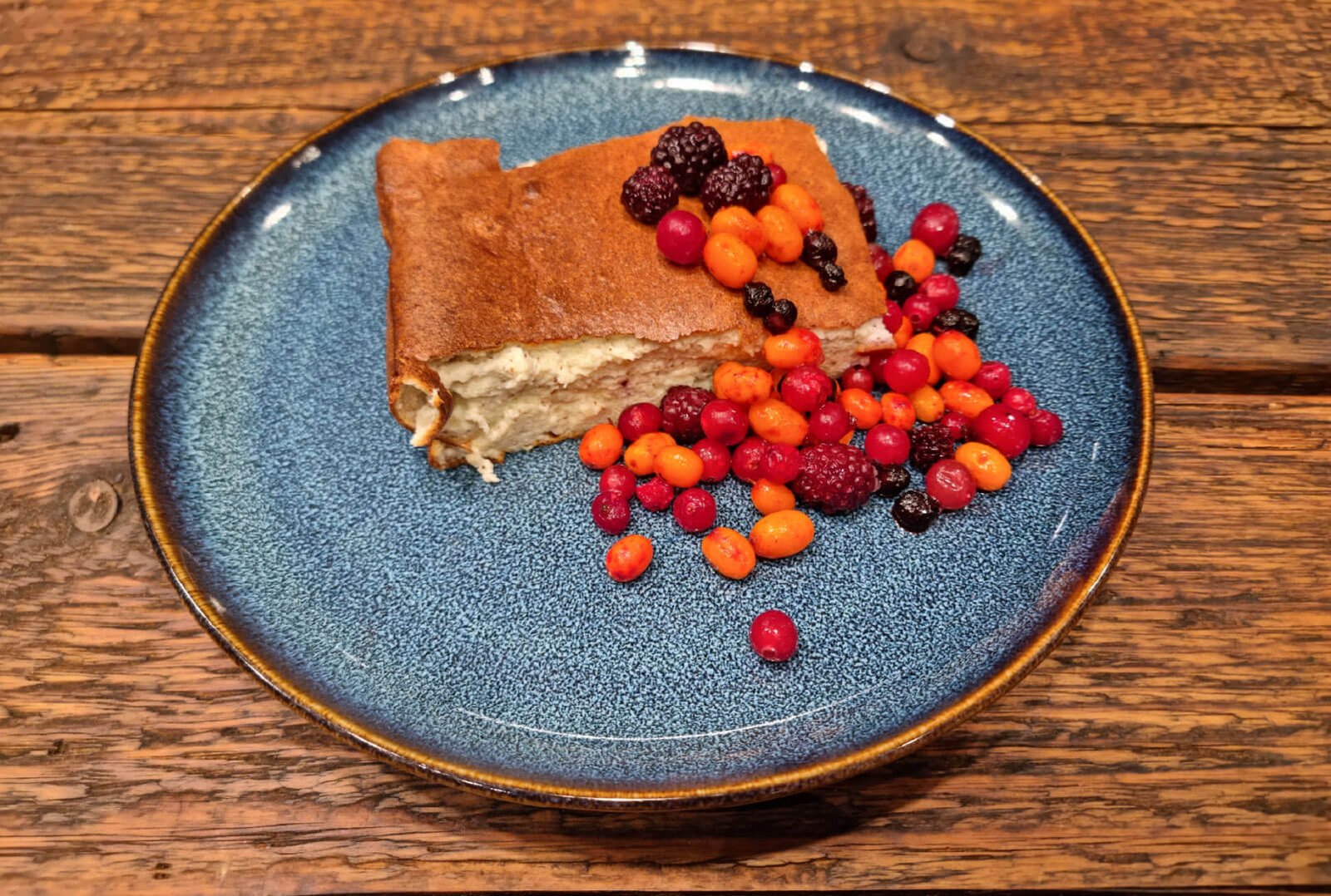Slice of cottage cheese bake served on a blue plate with a mix of colorful berries on top.